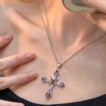 Silver cross necklace with pink stones worn by a person
